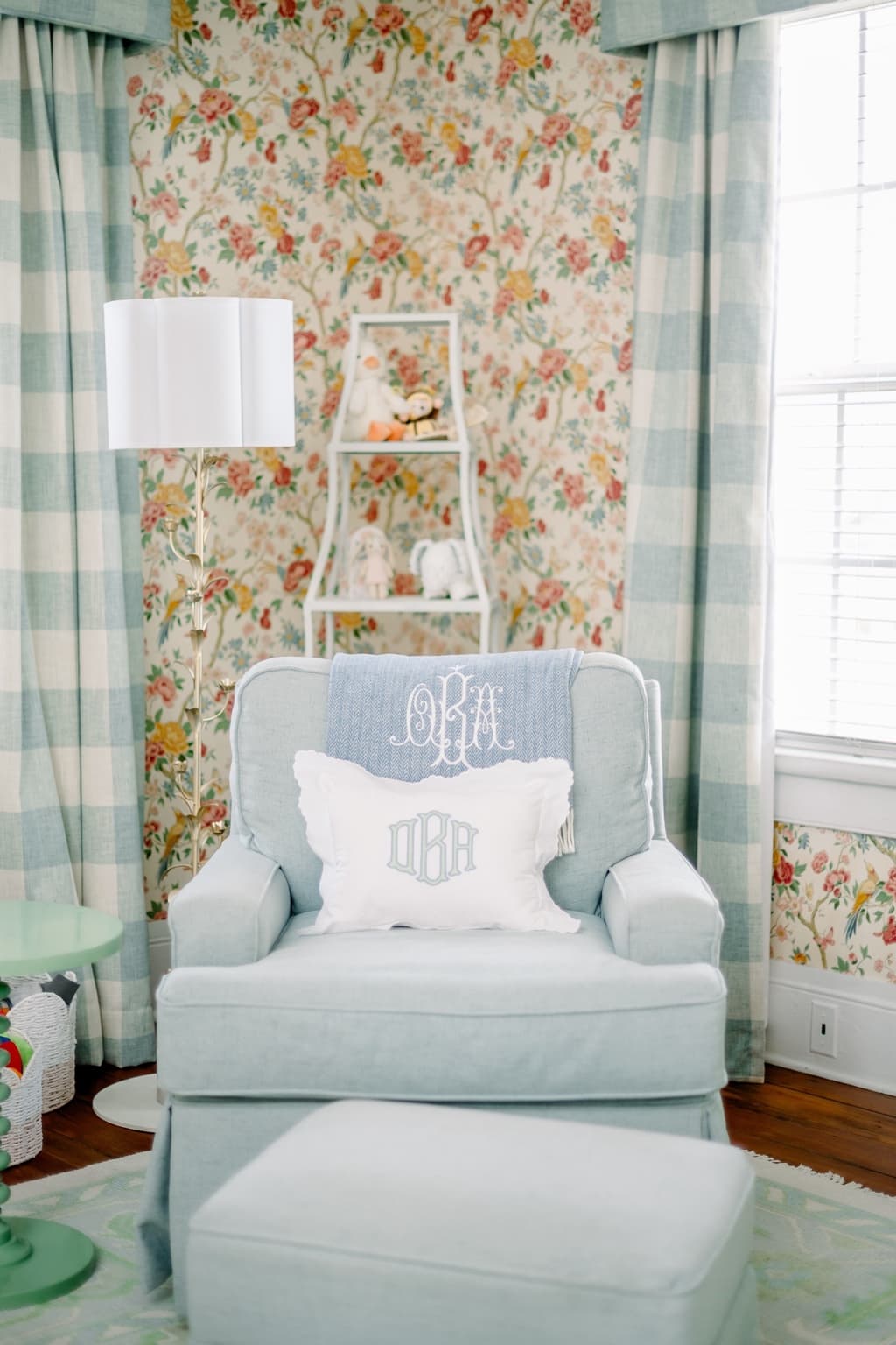 A blue chair framed by floral wallpaper and soft window treatments.